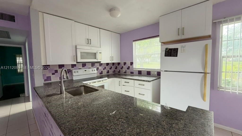 Kitchen featuring white shaker-style cabinetry, stone-finish countertops, an undermount stainless steel sink with a high-arch faucet, a mosaic tile backsplash, and white major appliances