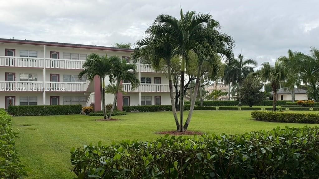 Exterior facade featuring a three-story multi-unit structure with tiered balconies, manicured lawn, mature palm trees, and perimeter shrubbery