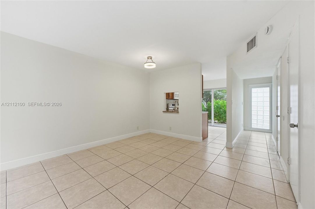 Neutral-toned interior space featuring light-colored ceramic tile flooring, a pass-through window to the kitchen, a contemporary flush-mount ceiling fixture, and a glass-paneled exterior door
