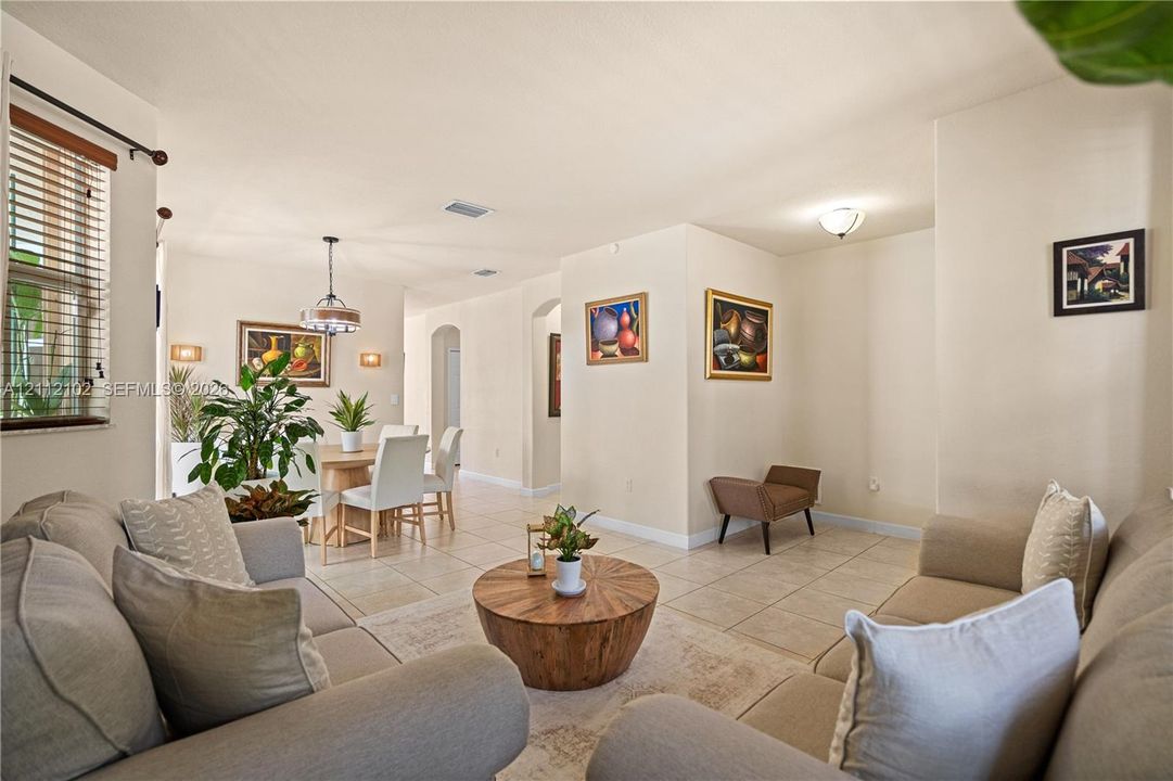 Open-concept living space featuring large-format ceramic tile flooring, neutral wall tones, arched wall openings, a pendant light fixture, and horizontal blind window treatments