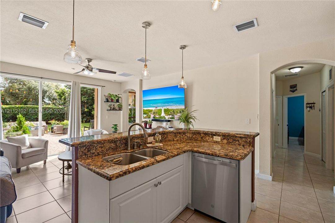 Kitchen featuring a multi-level stone countertop, dual basin undermount sink, stainless steel dishwasher, glass pendant lighting, and neutral cabinetry