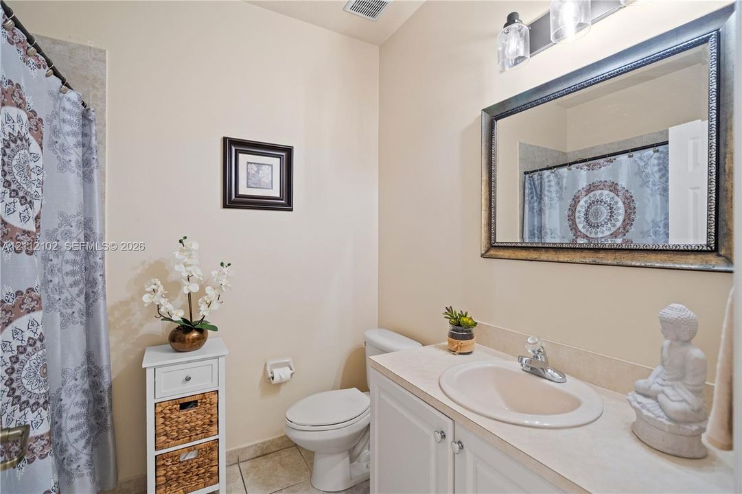 Bathroom featuring a vanity with a solid-surface countertop, an integrated sink with a chrome faucet, a rectangular wall mirror with a metallic frame, and a three-light fixture