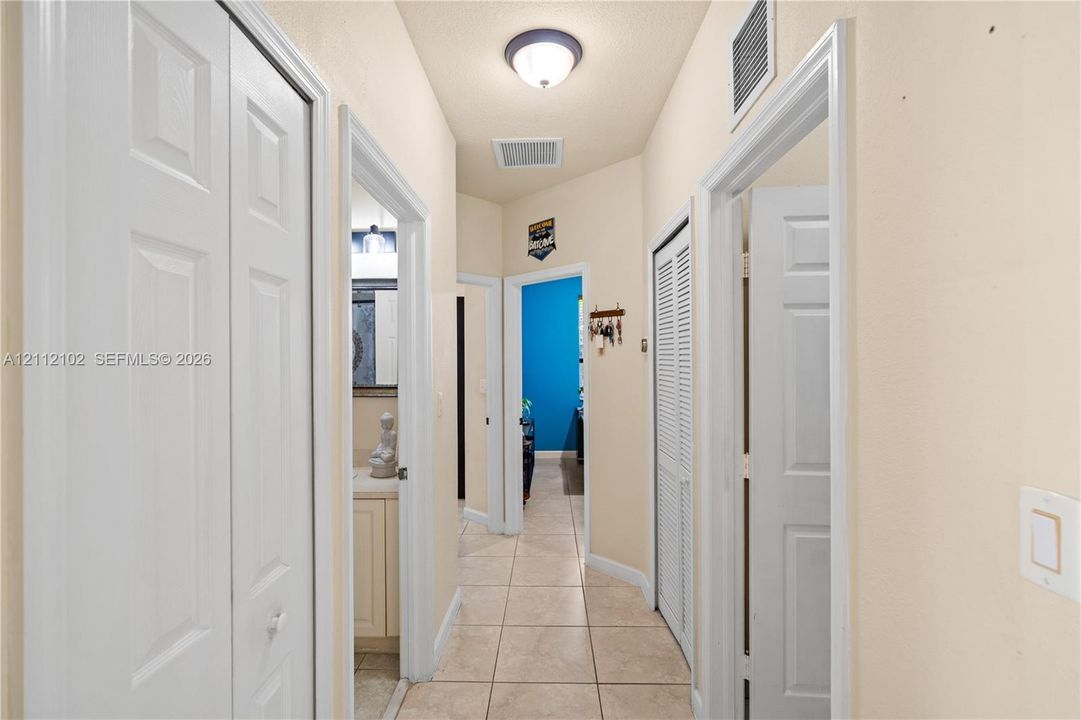Hallway featuring neutral-toned tile flooring, dual louvered-panel closets, and a flush-mount ceiling light fixture