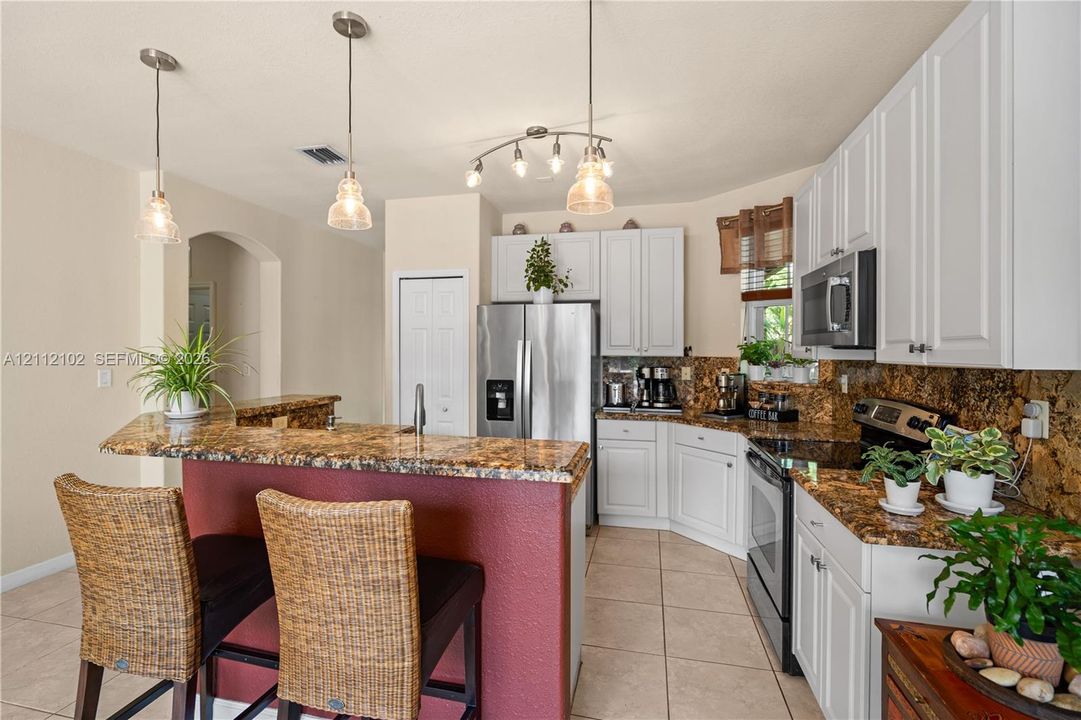 Kitchen featuring white cabinetry, stone-finish countertops, stainless steel appliances, ceramic tile flooring, and multi-light pendant fixtures