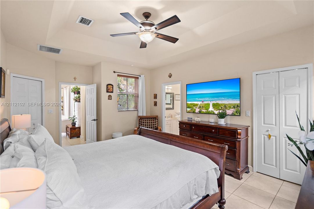 Tray ceiling, central ceiling fan, tile flooring, and dual bi-fold closet doors
