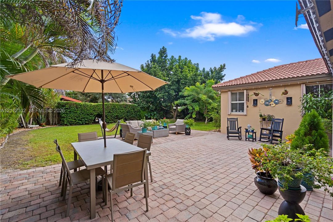 Spacious backyard featuring a paved patio, manicured lawn, perimeter landscaping, and tile roofline
