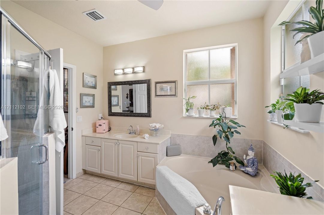 Bathroom featuring a tiled shower enclosure, vanity with integrated basin and stone countertop, soaking tub with tile surround, and floating shelving