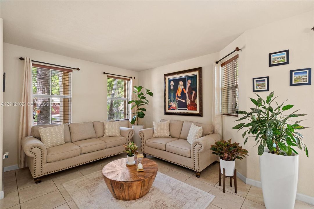 Living area featuring tile flooring, neutral wall tones, and three multi-pane windows with horizontal blinds