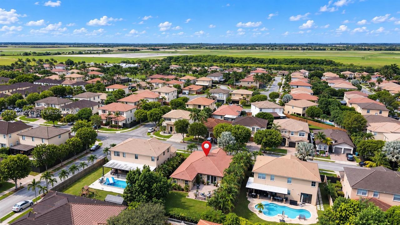 Aerial perspective featuring a tile-roof residence situated in a suburban community with established landscaping and expansive open-space surroundings