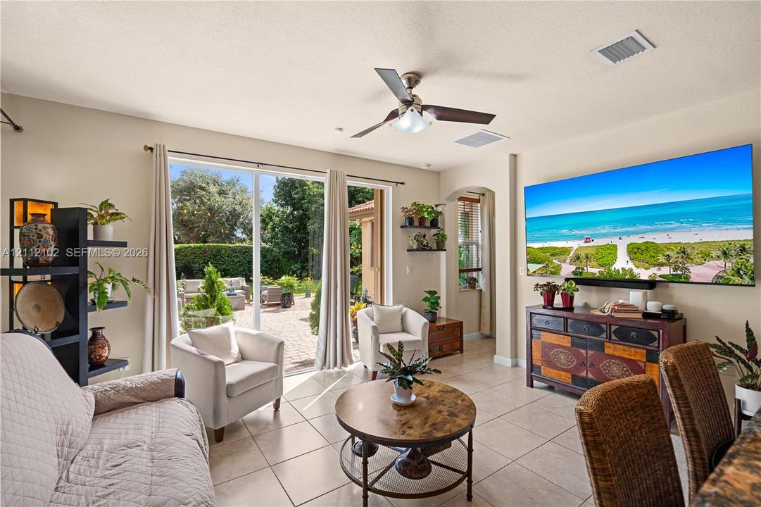 Living area featuring large-format ceramic tile flooring, a multi-speed ceiling fan with integrated lighting, and full-height sliding glass doors opening to a paved patio