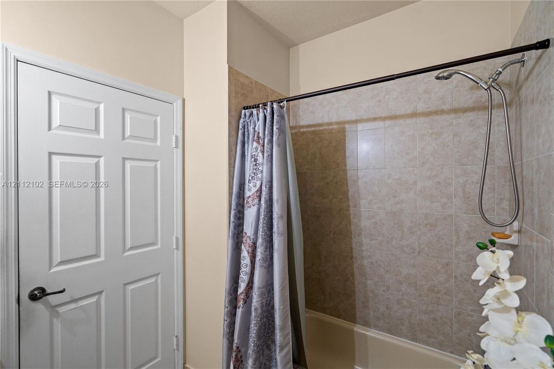 Bathroom featuring a white six-panel door with dark hardware, a bathtub with neutral-toned tiled surround, and a chrome handheld shower fixture