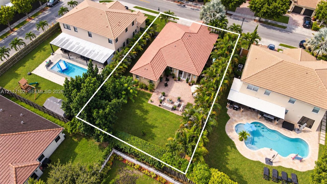 Aerial perspective featuring a tile roof, paved patio, and manicured lawn enclosed by perimeter landscaping