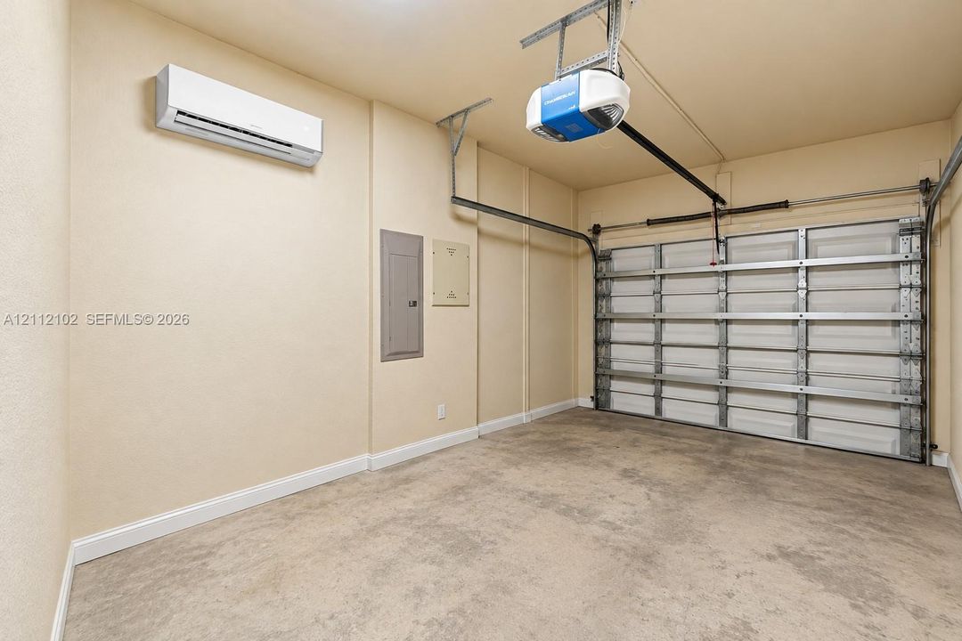 Garage interior featuring a concrete floor, wall-mounted ductless mini-split system, automated garage door opener, and integrated electrical service panel