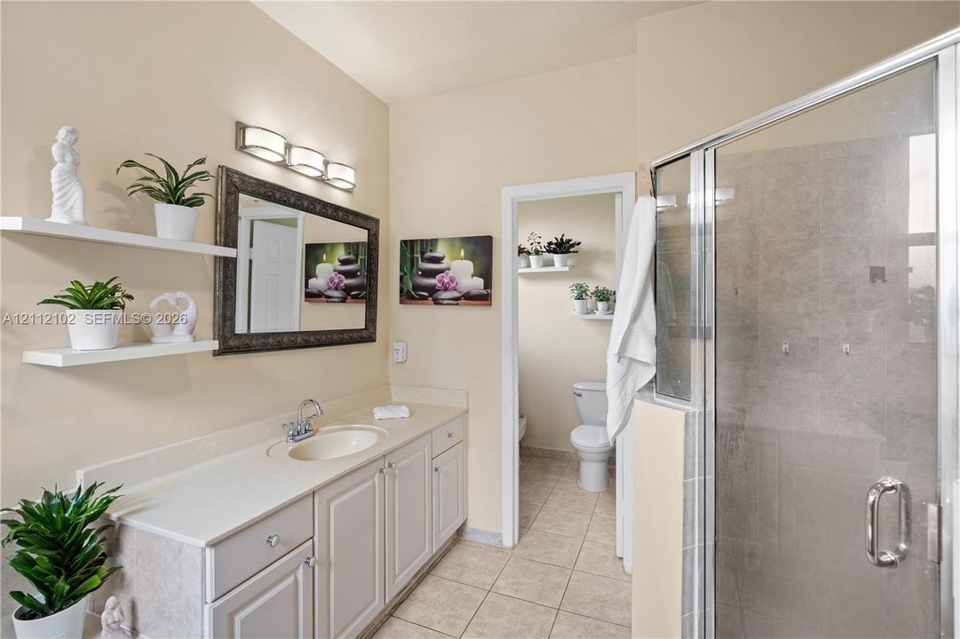 Vanity featuring white cabinetry, a solid surface countertop with an integrated basin, triple-bulb vanity lighting, glass-enclosed shower with tiled surround, and wall-mounted shelving