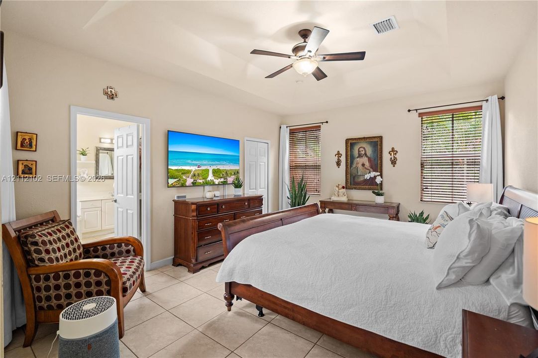 Tray ceiling with a central ceiling fan, neutral tile flooring, and dual windows with adjustable blinds