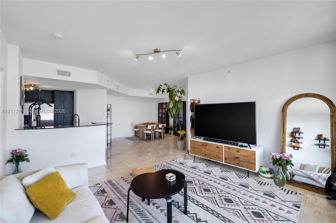 Open-concept interior featuring light stone flooring, recessed track lighting, and a kitchen peninsula with a dark stone countertop