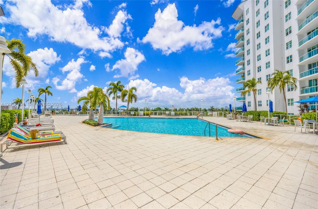 Swimming pool with tiled decking, mature palm trees, and perimeter fencing