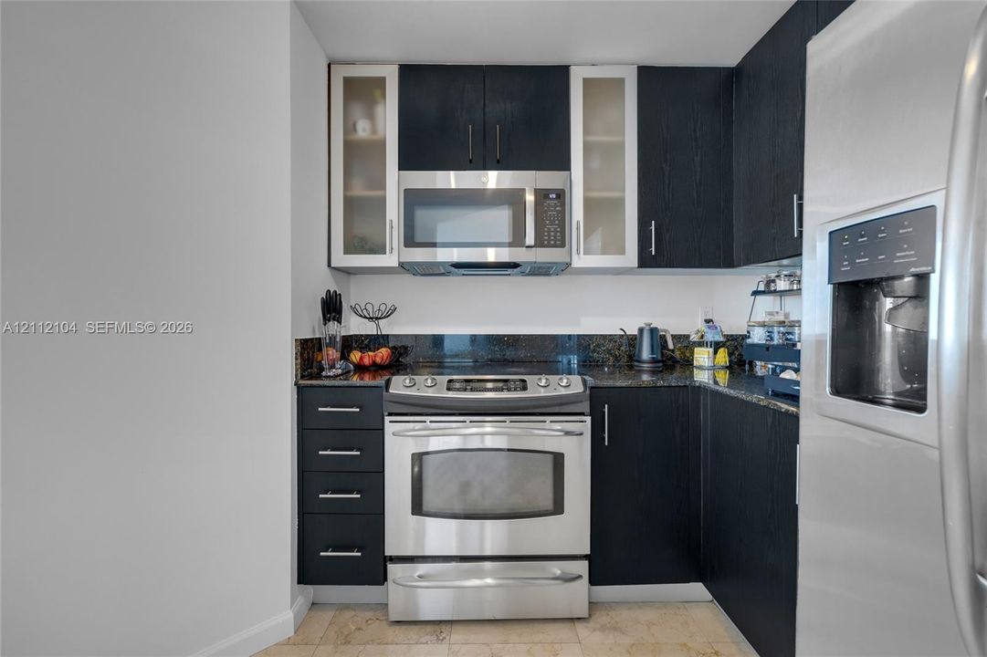 Kitchen featuring dark wood-finish cabinetry, glass-panel upper cabinets, stainless steel appliances, and dark stone-finish countertops