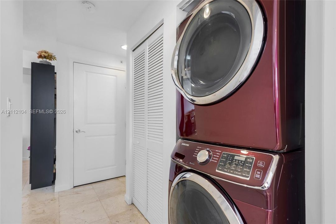 Laundry closet featuring a stackable washer and dryer set, white louvered doors, and stone-finish flooring