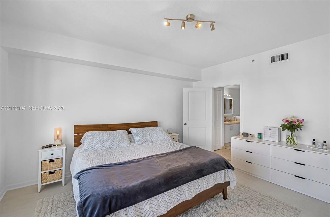Neutral-toned bedroom featuring minimalist interior design, four-bulb track lighting, and solid core interior door