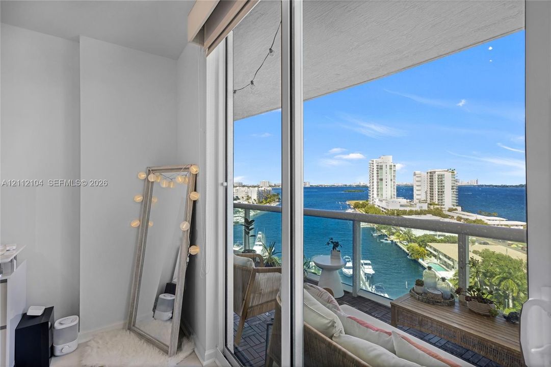 Full-height sliding glass doors opening to a private balcony with a metal and glass railing and expansive water, marina, and city skyline scenery