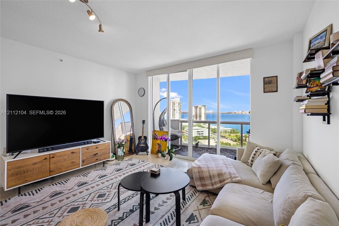 Floor-to-ceiling glass sliding doors, private balcony, neutral wall finishes, and adjustable track lighting