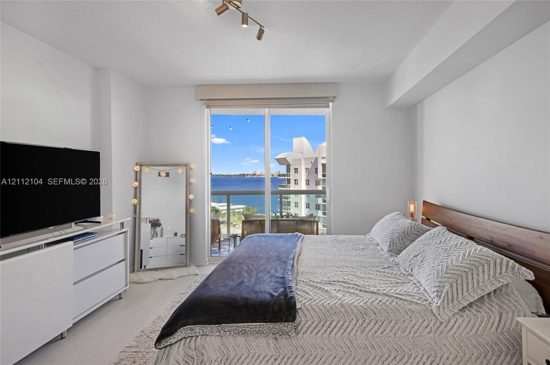 Sliding glass door with integrated window treatment, multi-light ceiling-mounted fixture, and water-facing balcony