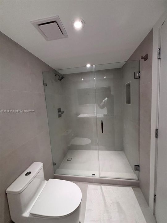Walk-in shower featuring a frameless glass enclosure, neutral large-format tile wall surrounds, built-in recessed wall niche, and integrated shower fixtures