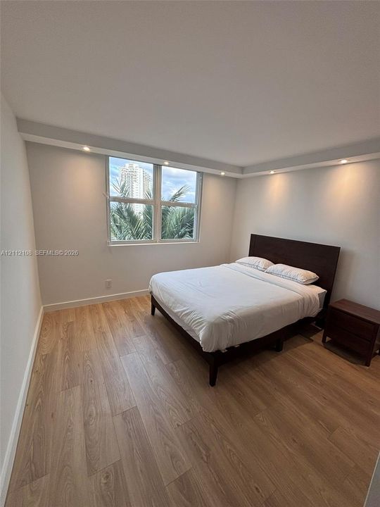 Neutral-toned room featuring wood-finish flooring, recessed perimeter ceiling lighting, and windows with exterior greenery