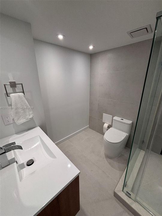 Modern vanity with a rectangular sink, quartz countertop, recessed ceiling lighting, large-format tile flooring, and a glass-enclosed shower