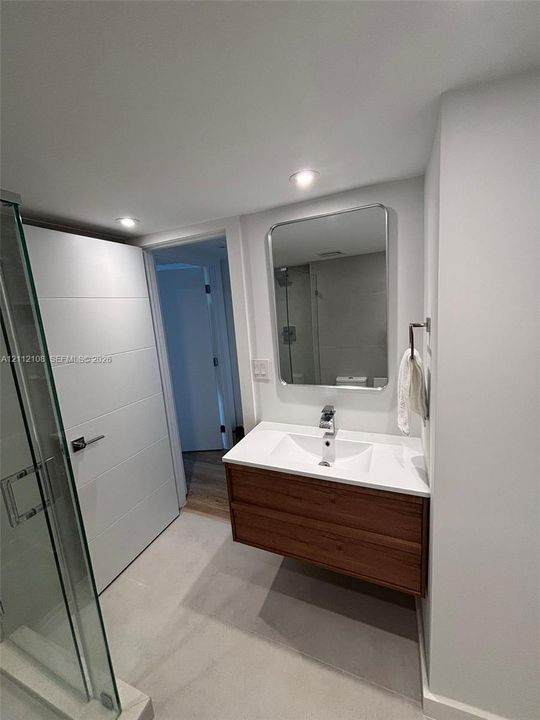 Floating wood-finish vanity with a white integrated basin, polished chrome faucet, and rectangular mirror