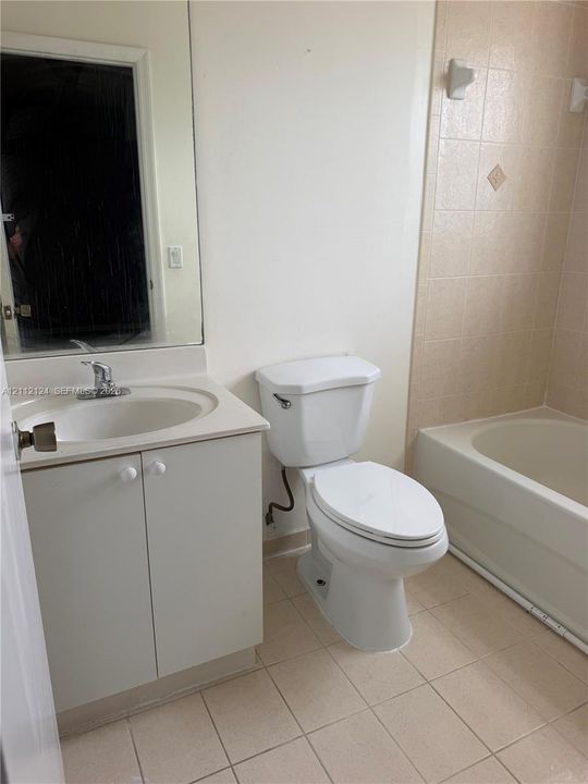 Bathroom featuring a vanity with an integrated sink, expansive wall-mounted mirror, ceramic tile flooring, and a tiled tub surround