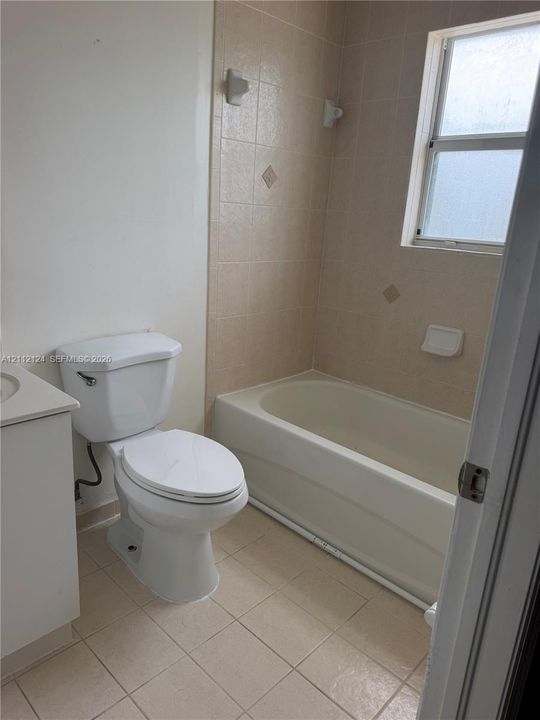 Bathroom featuring a built-in bathtub with tiled surround, light-colored floor tiling, and wall-mounted light fixtures