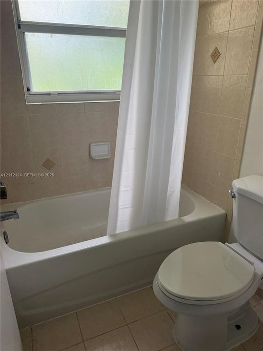 Bathtub with ceramic tile surround, integrated soap dish, privacy window, and standard toilet