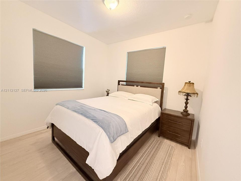 Neutral walls, light-toned wood-finish flooring, dual windows with fitted cellular shades, and a central ceiling-mounted light fixture