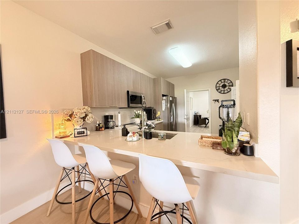 Kitchen featuring flat-panel wood-finish cabinetry, neutral solid-surface countertops, integrated breakfast bar, and stainless steel appliances