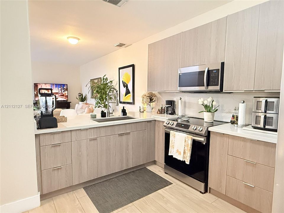 Kitchen featuring flat-panel wood-finish cabinetry, quartz countertops, stainless steel appliances, a deep undermount sink, and wood-finish flooring