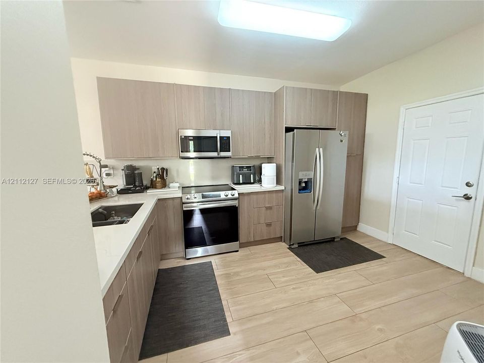 Kitchen featuring flat-panel wood-finish cabinetry, light-toned stone countertops, stainless steel appliances, and wood-finish flooring