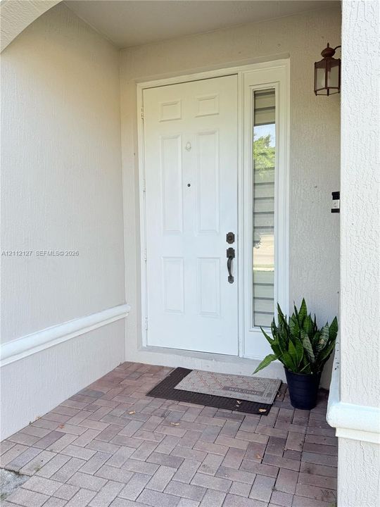 Covered entryway featuring a brick-paver porch, six-panel door with a sidelight, and an attached wall-mounted lantern fixture