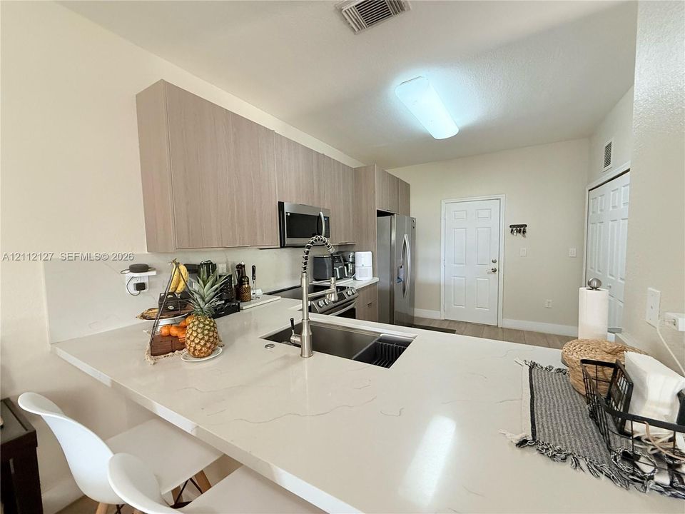 Kitchen featuring stone-finish countertops, wood-finish flat-panel cabinetry, stainless steel appliances, and a gooseneck faucet with an integrated sink