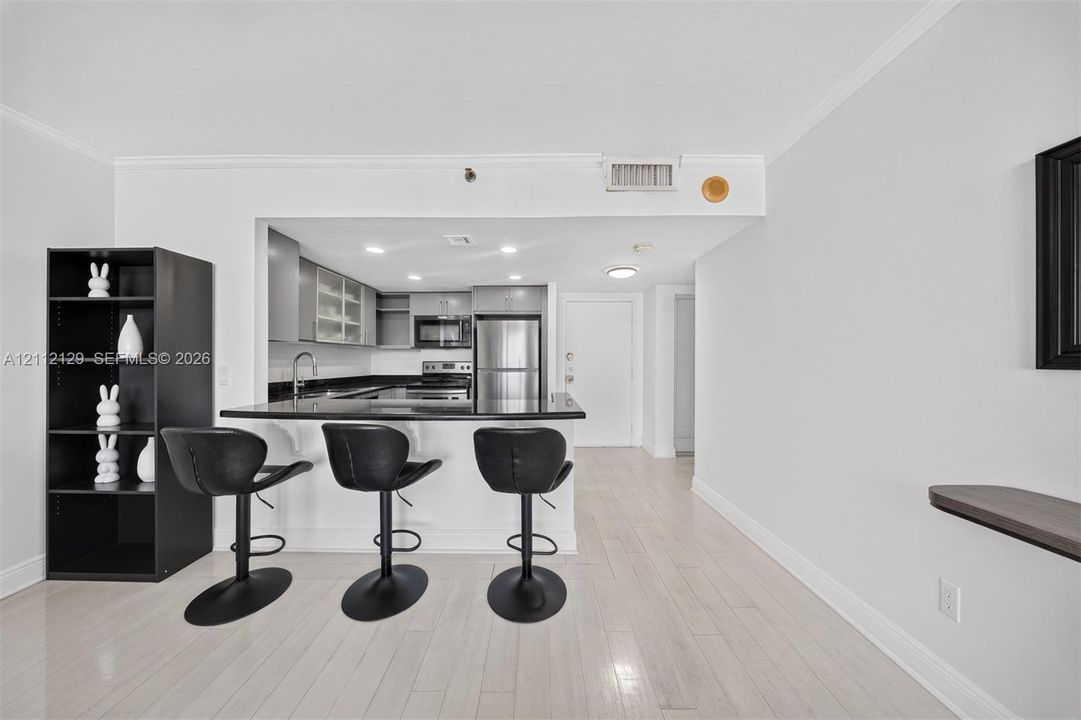 Kitchen featuring stone countertops, stainless steel appliances, cabinetry with frosted-glass panel doors, a breakfast bar, and light-toned flooring