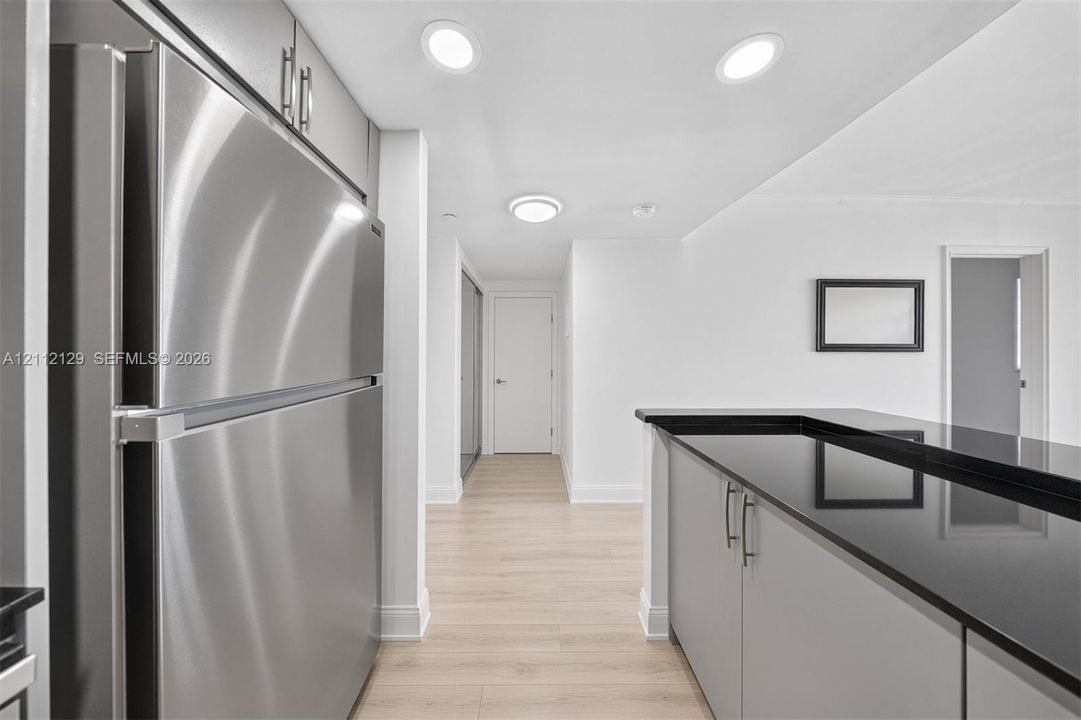 Kitchen featuring stainless steel refrigerator, dark stone-finish countertops, light wood-finish flooring, and recessed ceiling lighting