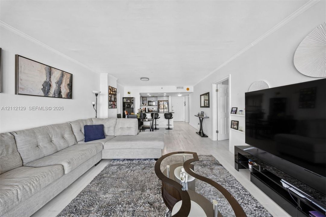 Open-concept living space featuring wood-finish flooring, white walls, and crown molding