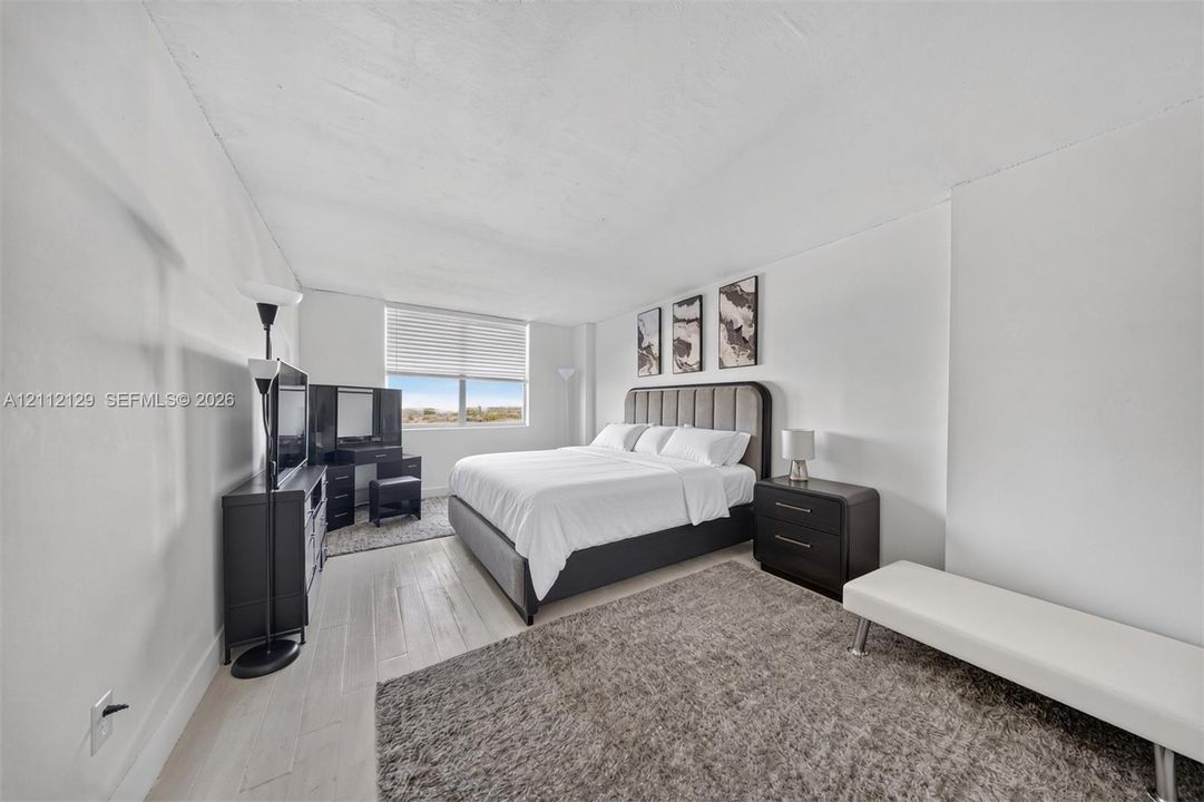 Spacious room featuring wood-finish flooring, a large window with horizontal blinds, and a smooth ceiling finish