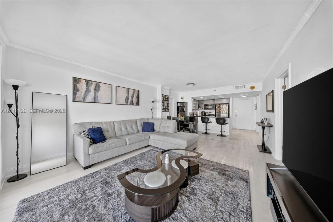 Open-concept living space featuring wood-finish flooring, recessed lighting, and a kitchen equipped with a breakfast bar, stone-surface countertops, and stainless steel appliances