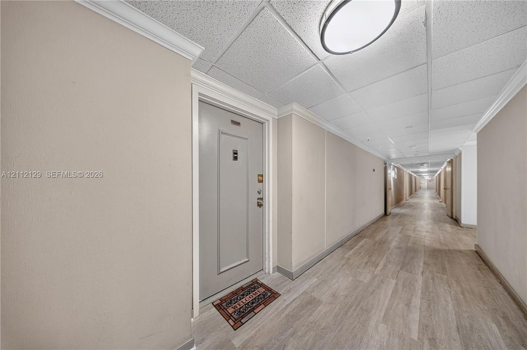 Hallway featuring wood-finish flooring, neutral-toned walls, crown molding, and flush-mount ceiling lighting