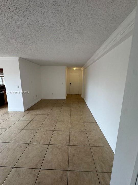 Open interior space featuring large-format neutral floor tile, crown molding, and textured ceiling finish