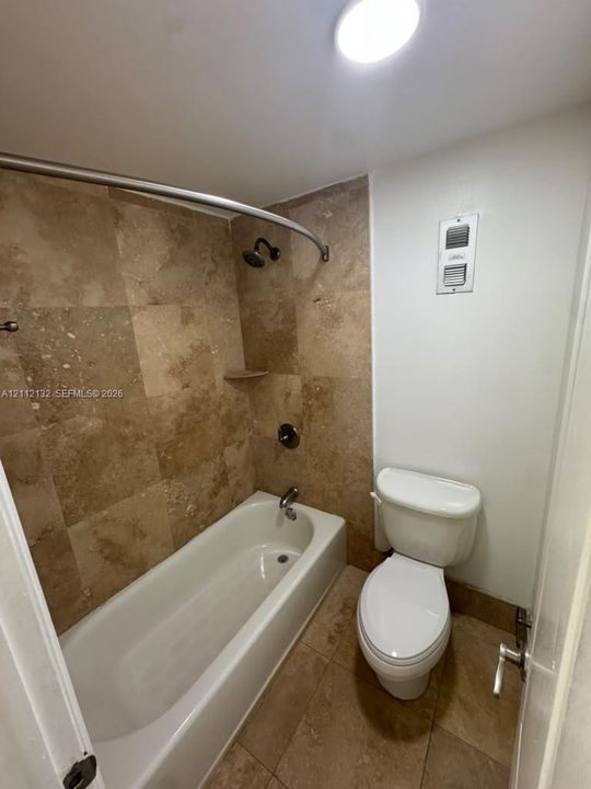 Full bathroom featuring stone-tiled walls, a built-in bathtub, a curved shower rod, and stone-tiled flooring