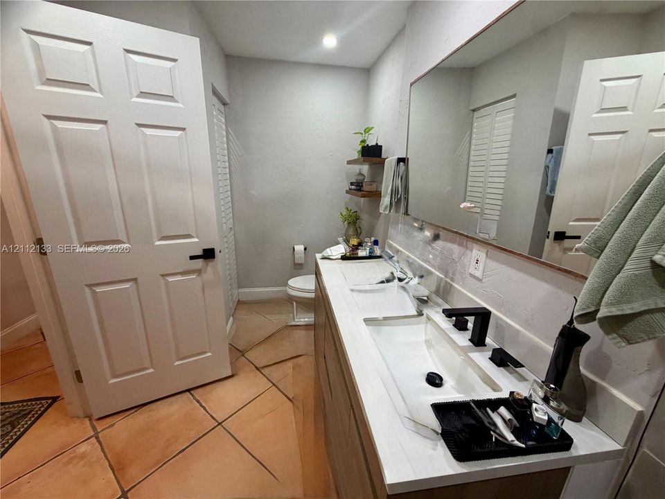 Dual-sink vanity with wood-finish cabinetry, white countertop, matte black widespread faucets, and two built-in wood-finish floating shelves