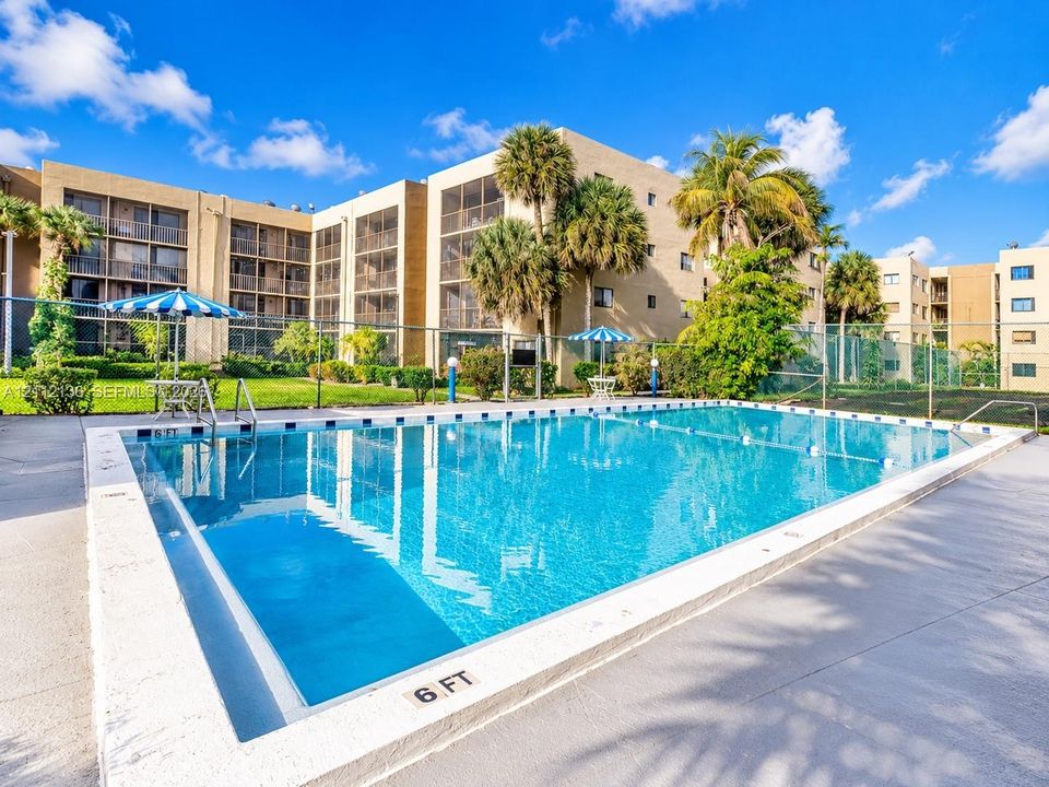 Outdoor swimming pool featuring a concrete deck, safety fencing, and mature landscaping